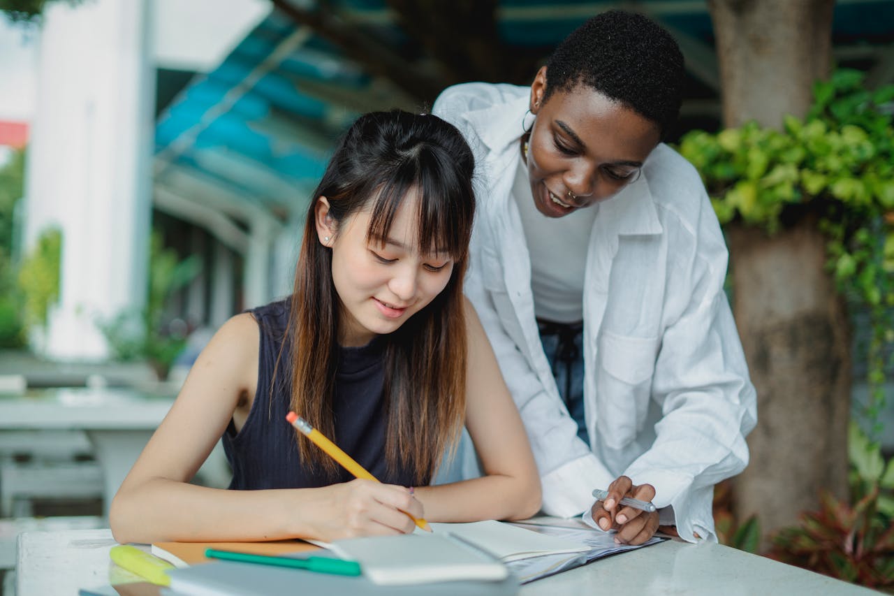 Two students working together outside, studying and discussing in a park setting.