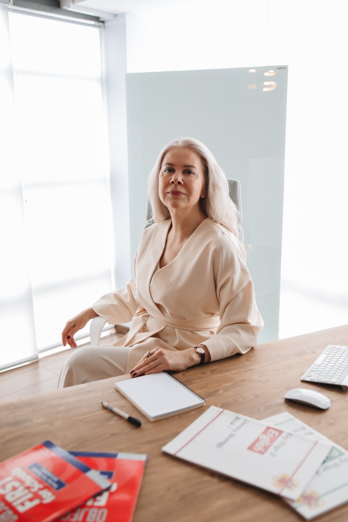 A woman sitting confidently at a desk in a bright, modern office space with documents and a notepad.