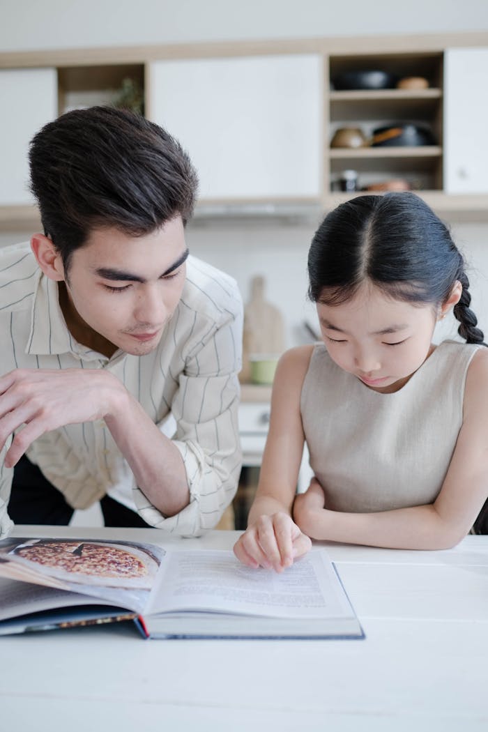 Father and daughter reading a cookbook together in a cozy kitchen setting, fostering learning and bonding.