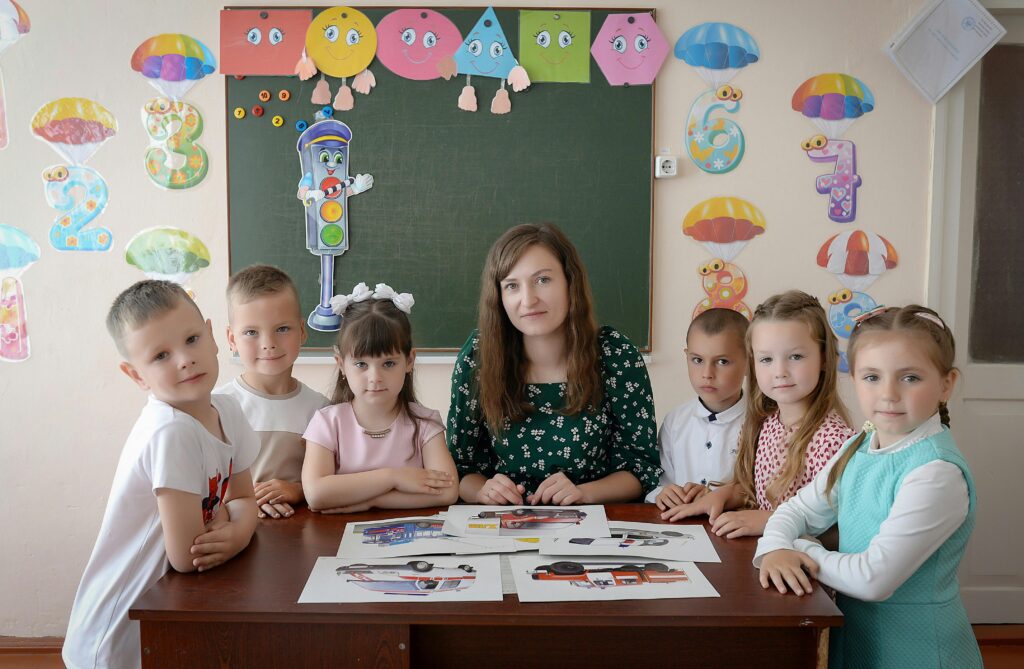 A group of children with their teacher in a vividly decorated classroom, learning together.