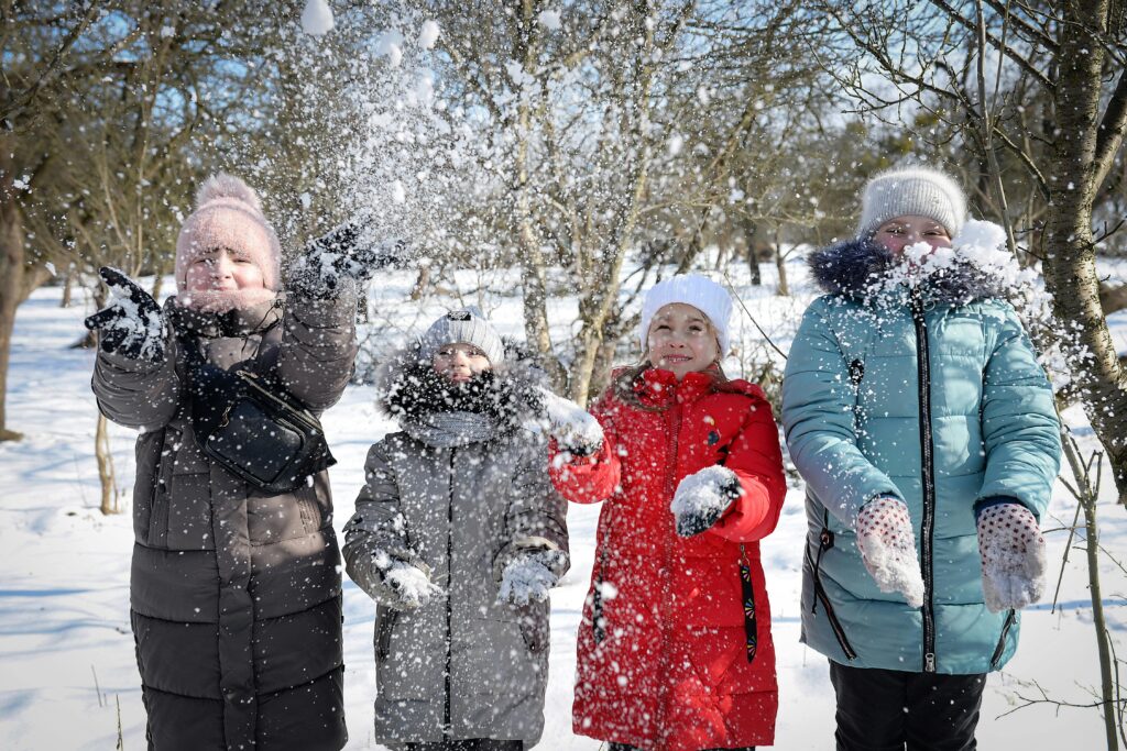 Four kids joyfully playing with snow in a winter landscape, wearing colorful winter clothes.
