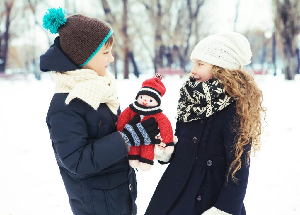 Two children in winter clothing enjoying a snowy day with a snowman toy.