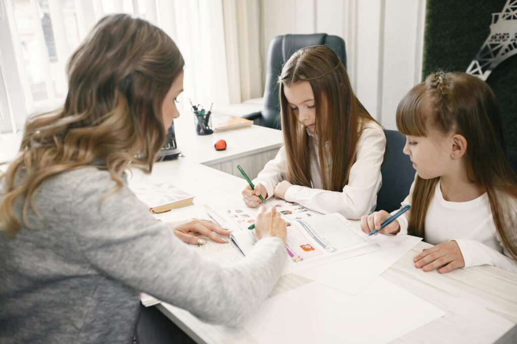 Woman teaching two girls in a bright office environment, focusing on an educational task together.