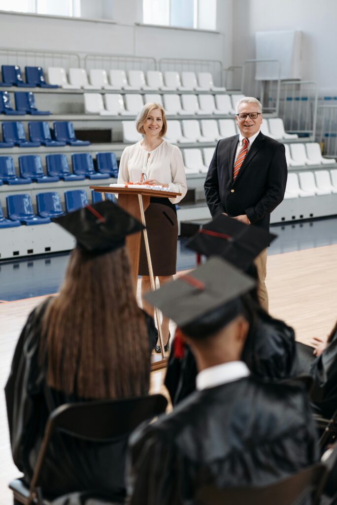 pexels-photo-7942498-7942498 A formal graduation ceremony in a gymnasium with two speakers addressing graduates.