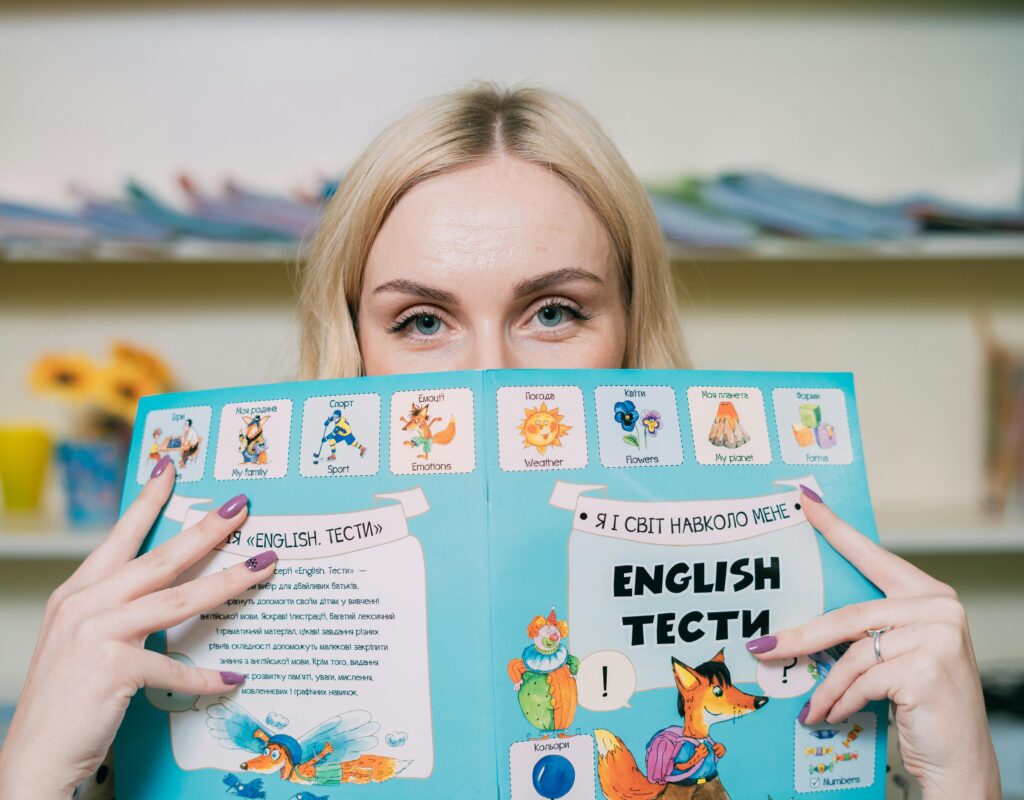 Blonde woman holding and reading an illustrated English book indoors.