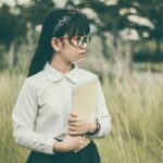 asian, student, book, child, girl, uniform, school uniform, eyeglasses, field, grass, nature, kid, looking away, outdoors, portrait